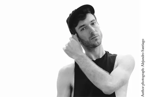 Author photo for Jordan Tannahill in black and white. Jordan stands looking into the camera contemplatively, holding onto his right ear with his left hand.